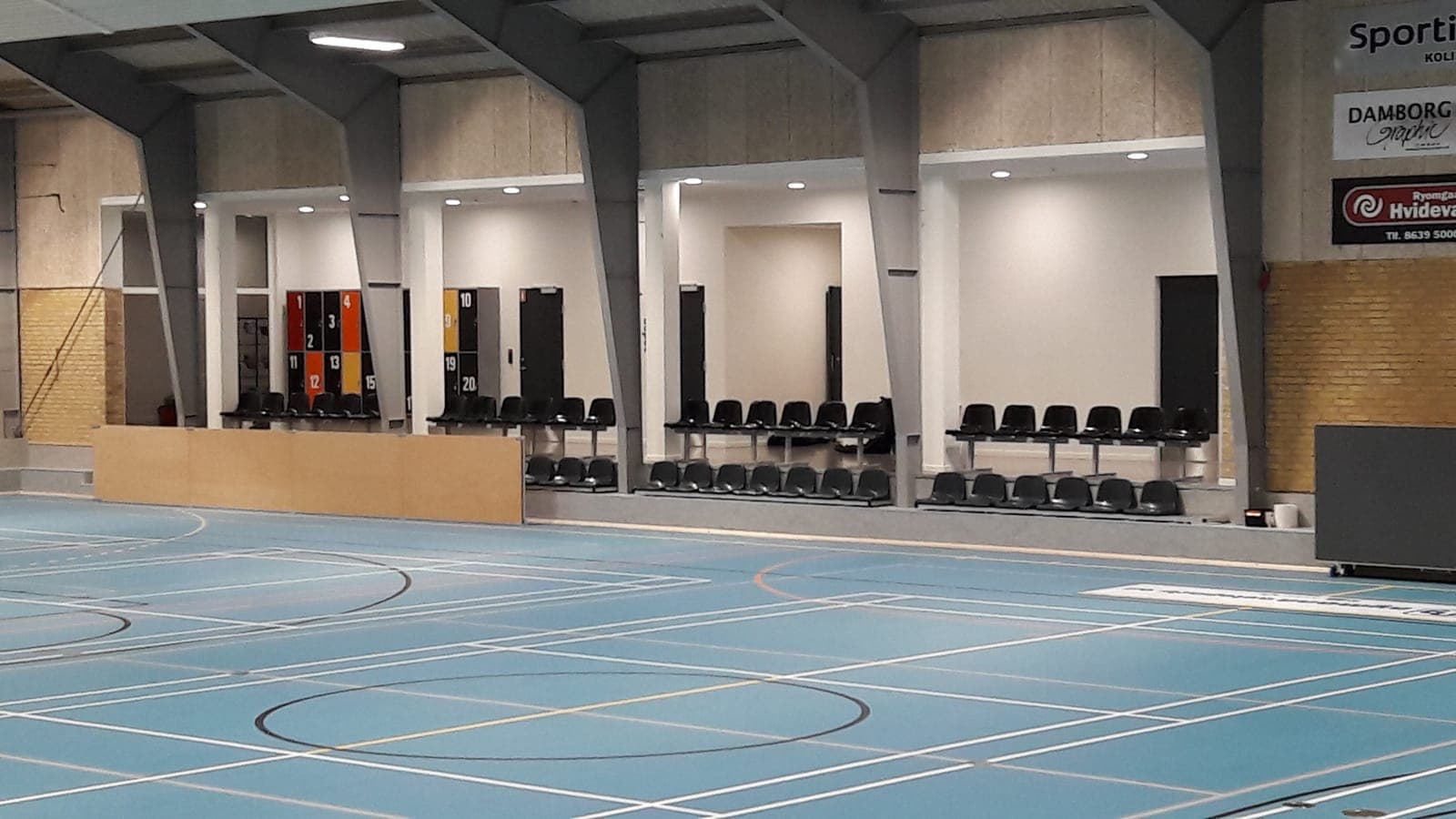 Overblik over Kolind Hallen med to rækker sorte tribunesæder langs banen
